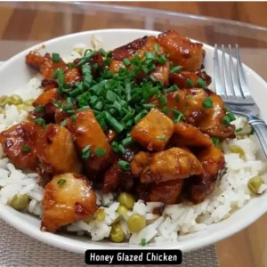 A plate of honey glazed chicken pieces garnished with sesame seeds and green onions