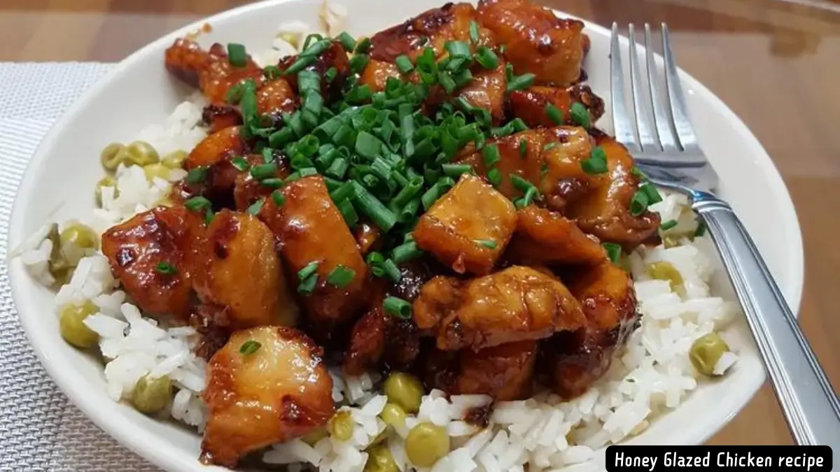 A close-up of honey glazed chicken pieces served over a bed of steamed rice with peas, garnished with chopped green onions.