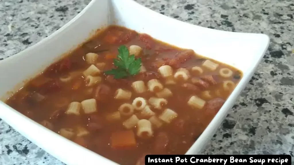 A bowl of Instant Pot Cranberry Bean Soup with pasta and a garnish of fresh parsley, served in a white square bowl on a granite countertop.