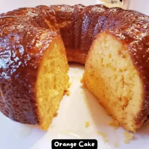 A beautifully glazed orange cake on a white serving platter, topped with a shiny orange glaze.