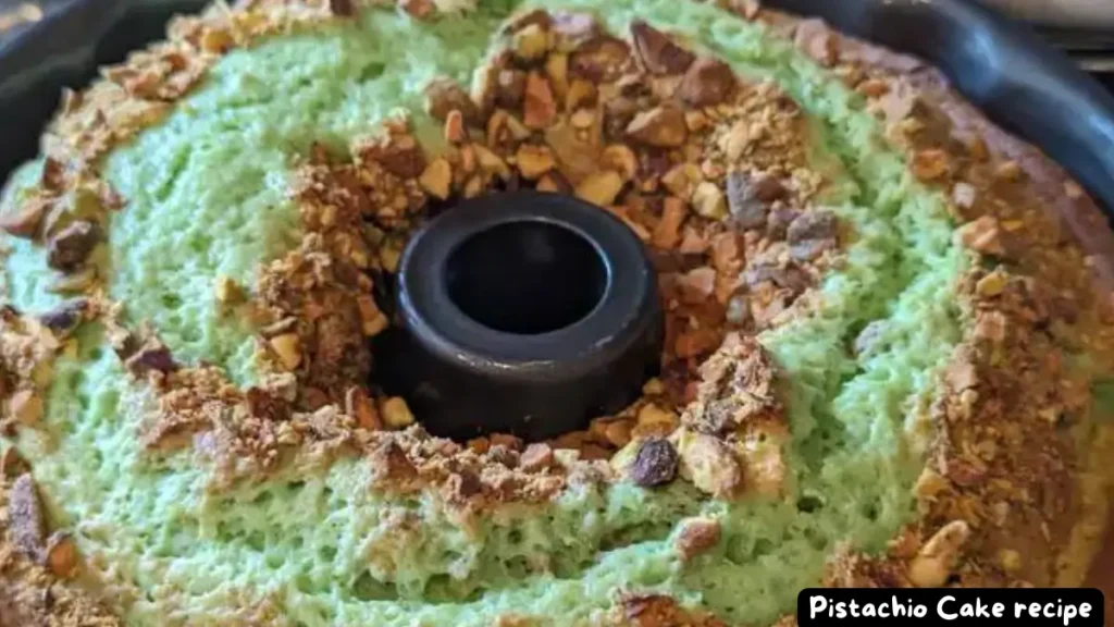 A freshly baked green pistachio Bundt cake topped with chopped pistachios, cooling in a Bundt pan.