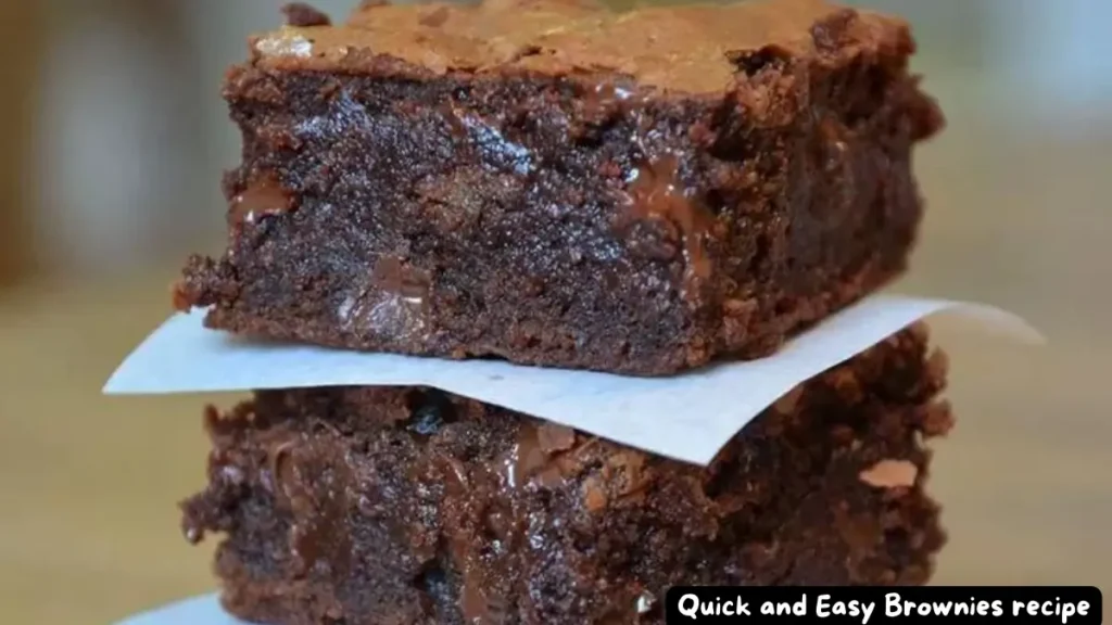 A close-up of two stacked, rich and gooey brownies with a glossy, cracked top.