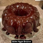 A close-up of a Double Chocolate Brownie Cake with a rich chocolate glaze dripping down the sides, displayed on a glass cake stand.