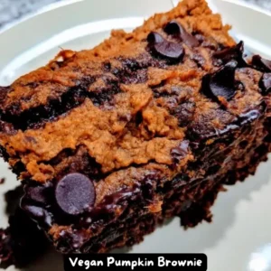 A delectable slice of vegan pumpkin brownie with a marbled pumpkin swirl on top, garnished with vegan coconut whipped cream.