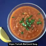 A bowl of Vegan Turkish Red Lentil Soup garnished with fresh parsley and a lemon wedge.