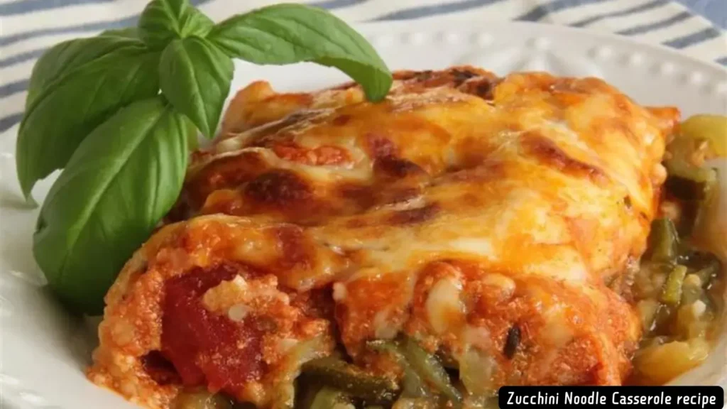 A serving of zucchini noodle casserole garnished with a fresh basil leaf on a white plate.