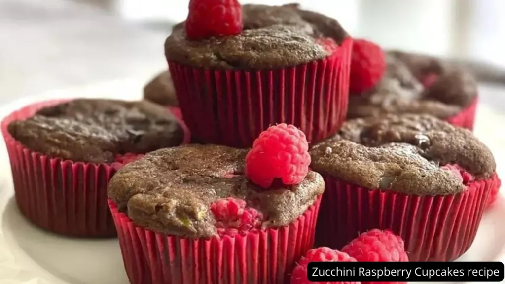 A close-up of moist and flavorful zucchini raspberry cupcakes topped with fresh raspberries, displayed on a white plate.