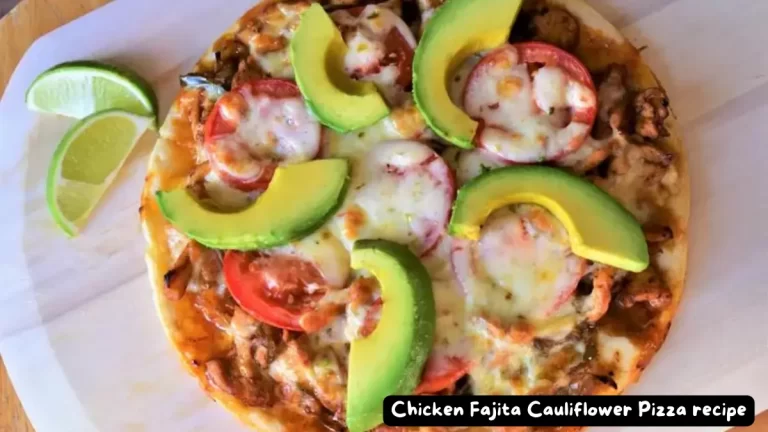 A top view of Chicken Fajita Cauliflower Pizza topped with slices of avocado and served with lime wedges on a parchment-lined board.