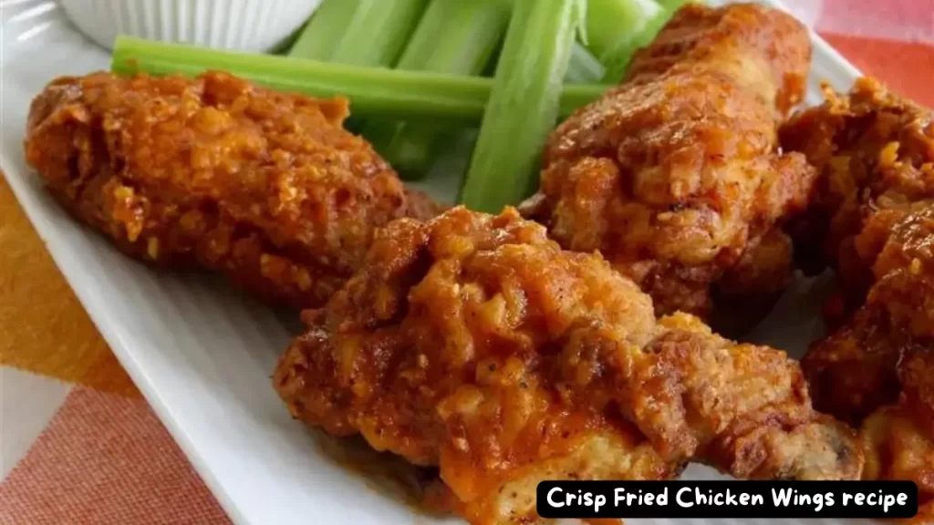 A close-up of perfectly crisp fried chicken wings with a golden-brown coating, served with celery sticks and a dipping sauce.