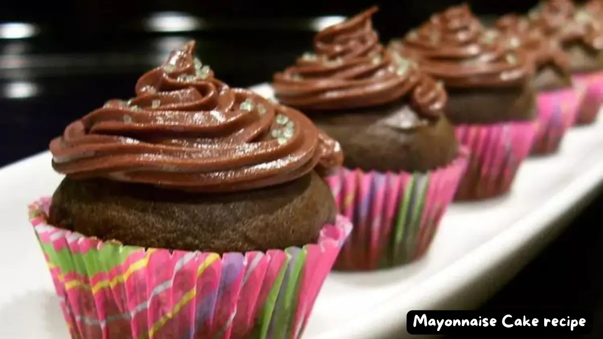 A close-up of chocolate cupcakes with swirled chocolate frosting, served in vibrant, multicolored cupcake liners, lined up on a white serving dish.