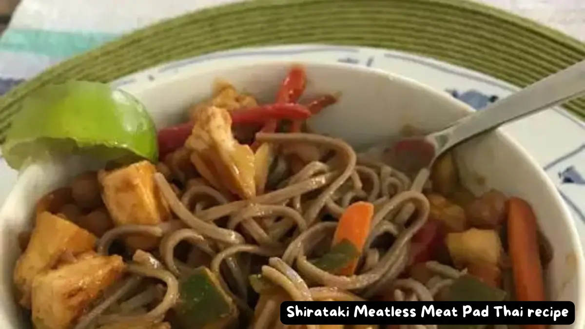 A close-up of a bowl of Shirataki Meatless Meat Pad Thai, featuring tofu chunks, vegetables, and lime wedge, garnished with fresh bean sprouts and chopped cashews.