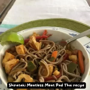 A vibrant bowl of Shirataki Meatless Meat Pad Thai garnished with bean sprouts, cashews, and lime wedges.