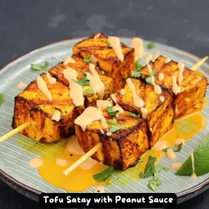 Grilled tofu skewers with peanut sauce served on a plate with lime wedges