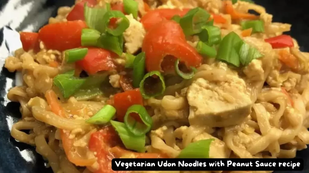 A bowl of vegetarian udon noodles with colorful vegetables and creamy peanut sauce