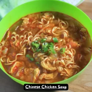 A bowl of Chinese chicken soup with ramen noodles, spiced with turmeric, ginger, and chile paste, garnished with green onions.