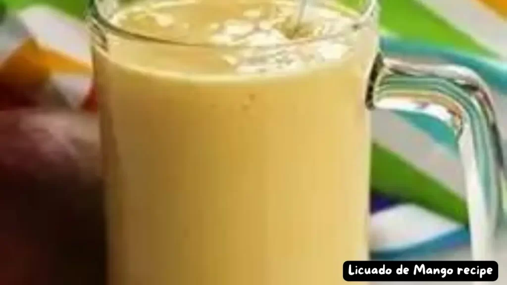Glass of Licuado de Mango, a creamy Mexican mango smoothie, with a straw on a colorful background.