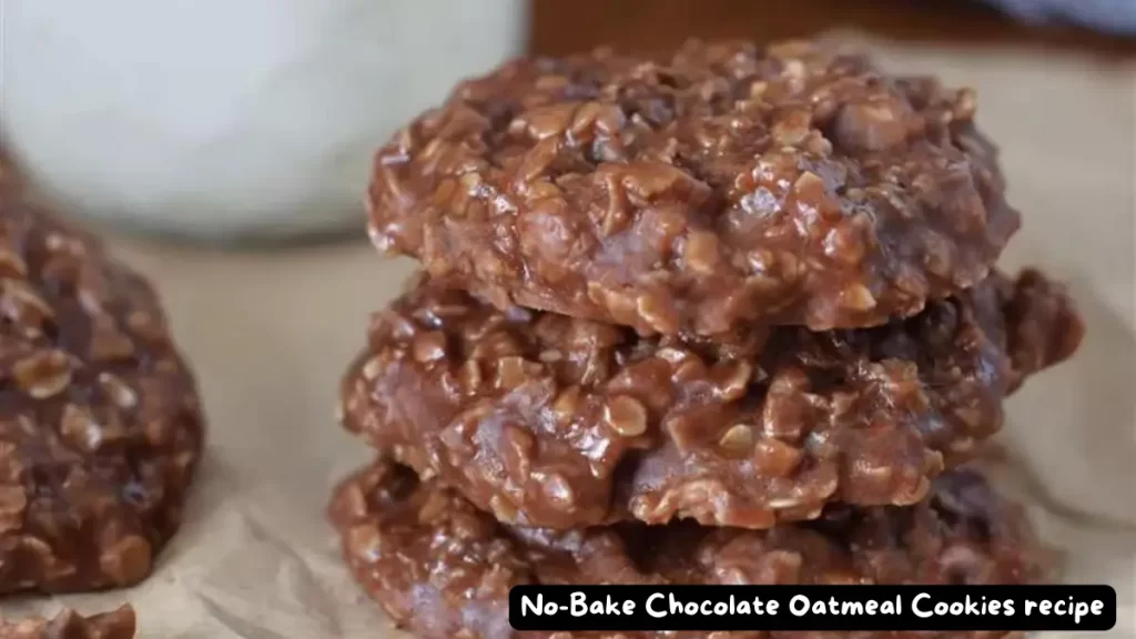 A close-up view of a stack of three no-bake chocolate oatmeal cookies on a parchment paper with a glass of milk in the background.