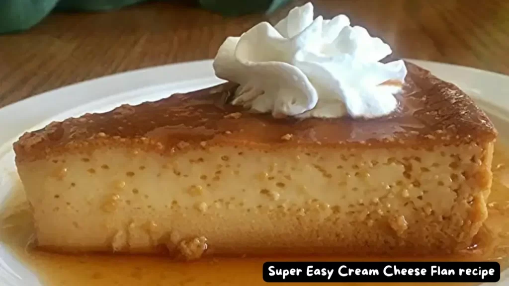 A close-up view of a slice of Super Easy Cream Cheese Flan topped with a swirl of whipped cream, served on a white plate with caramel sauce.