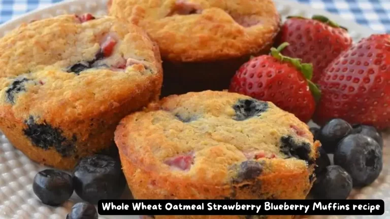 A close-up image of freshly baked whole wheat oatmeal strawberry blueberry muffins, showcasing their golden brown tops with strawberries and blueberries scattered around.