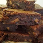 A tray of chunky fudge brownies cut into squares, with a gooey chocolate center and chunks of fudge visible.