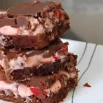 A close-up of Chocolate Cherry Chunk Brownies with layers of brownie, cherry filling, and smooth chocolate topping.