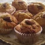 Freshly baked maple and pecan muffins with a pecan half topping, drizzled with syrup, and golden brown.