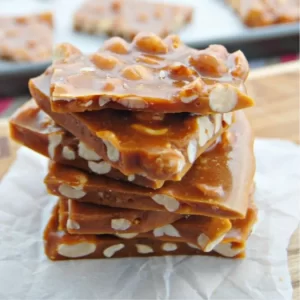 A tray of homemade peanut brittle cooling on parchment paper.