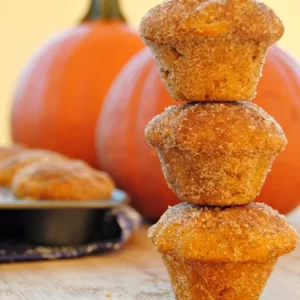 Golden pumpkin donut mini muffins coated with cinnamon-sugar resting on a cooling rack.