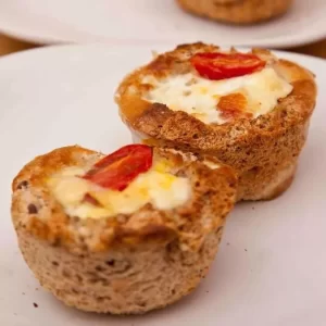 A plate of toast cups filled with eggs, sausage, and tomatoes, served in a muffin tin.