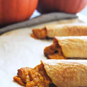 Crispy baked pumpkin flautas garnished with herbs, served on a white platter.